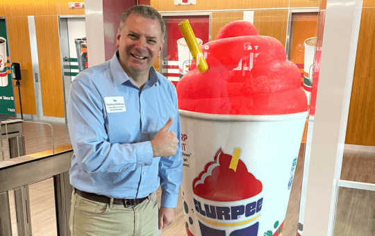 man standing holding his thumb up next to a giant slurpee snow cone