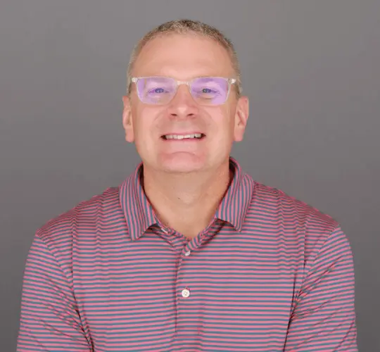 headshot of a man smiling with clear glasses wearing a striped polo shirt. 